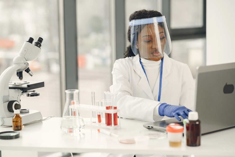 Laboratory research of blood, coronavirus concept. Afrcican woman inspecting blood and using laptop.