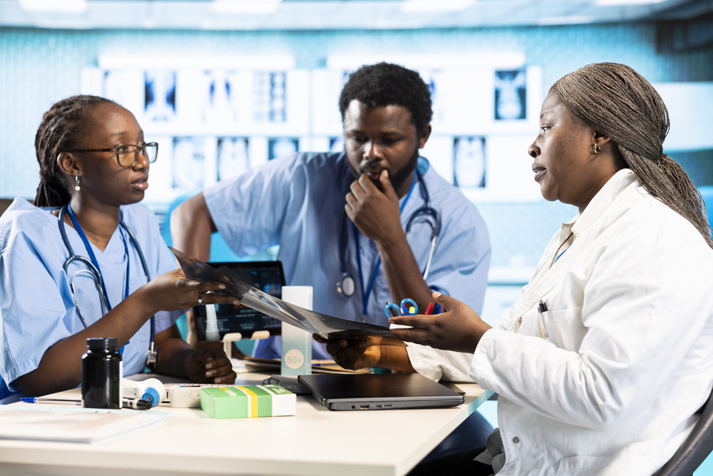 Black expert discussing with junior nurses to find the best treatment options, showcasing teamwork and professionalism in the healthcare industry. Improving the services at clinic.
